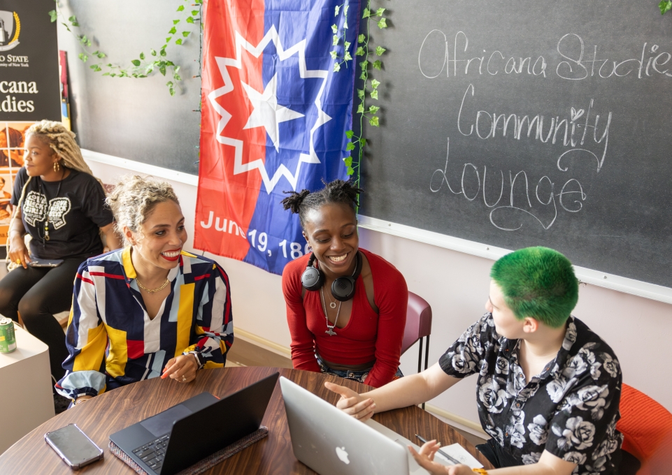 A professor sits and talks with two students in the Africana Studies community lounge